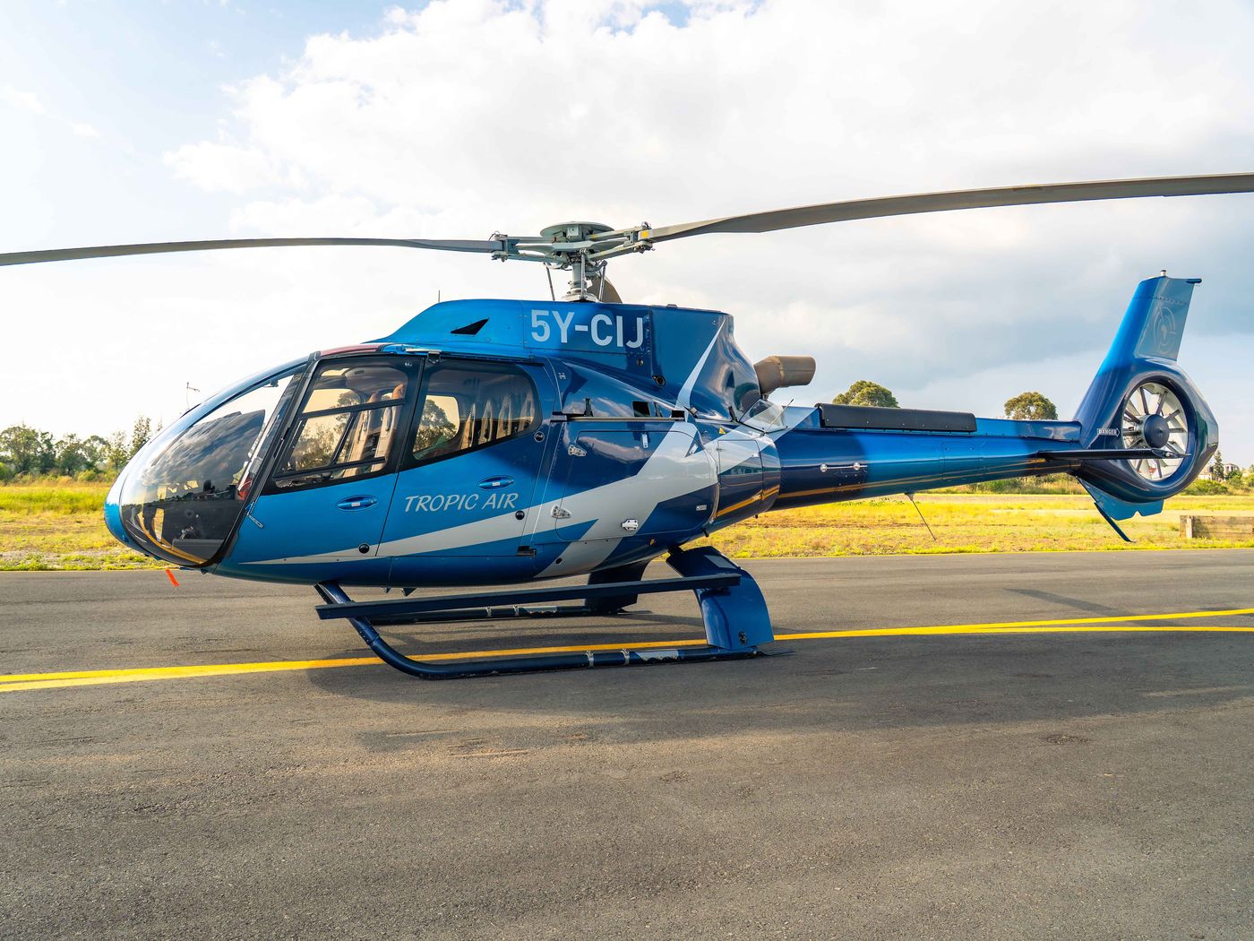 Tropic Air Airbus H130 helicopter parked on the tarmac, registration 5Y-CIJ, in blue Tropic Air livery